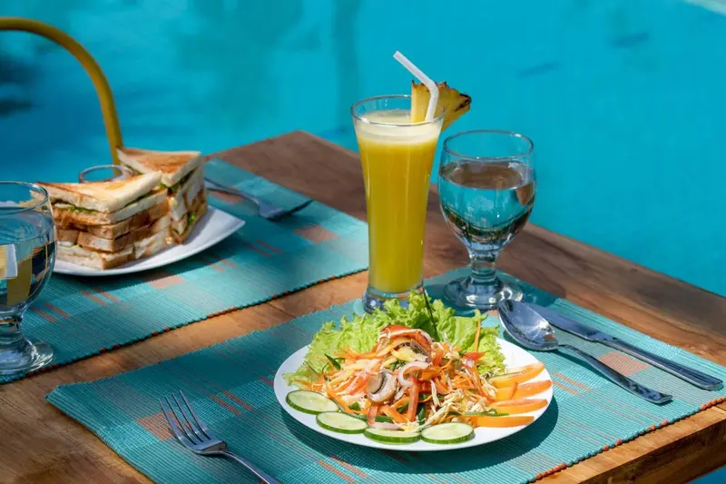 Une table en bois présente des plats colorés et des boissons au bord d'une piscine.