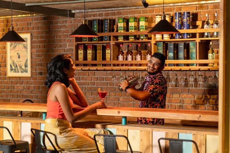 Un barman prépare un cocktail pour une cliente souriante dans un décor chaleureux.
