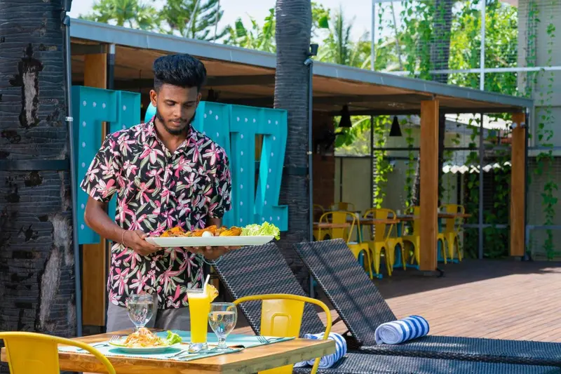 Un serveur présente un plateau de nourriture sur une terrasse ensoleillée.