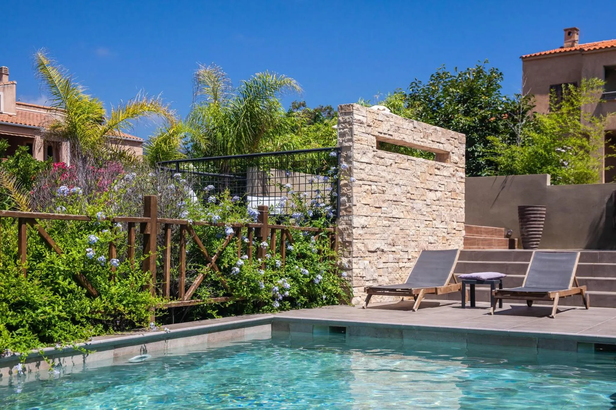 Deux transats sont installés au bord d'une piscine rectangulaire dans un jardin luxuriant.