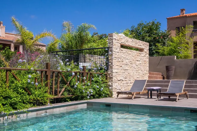 Deux transats sont installés au bord d'une piscine rectangulaire dans un jardin luxuriant.