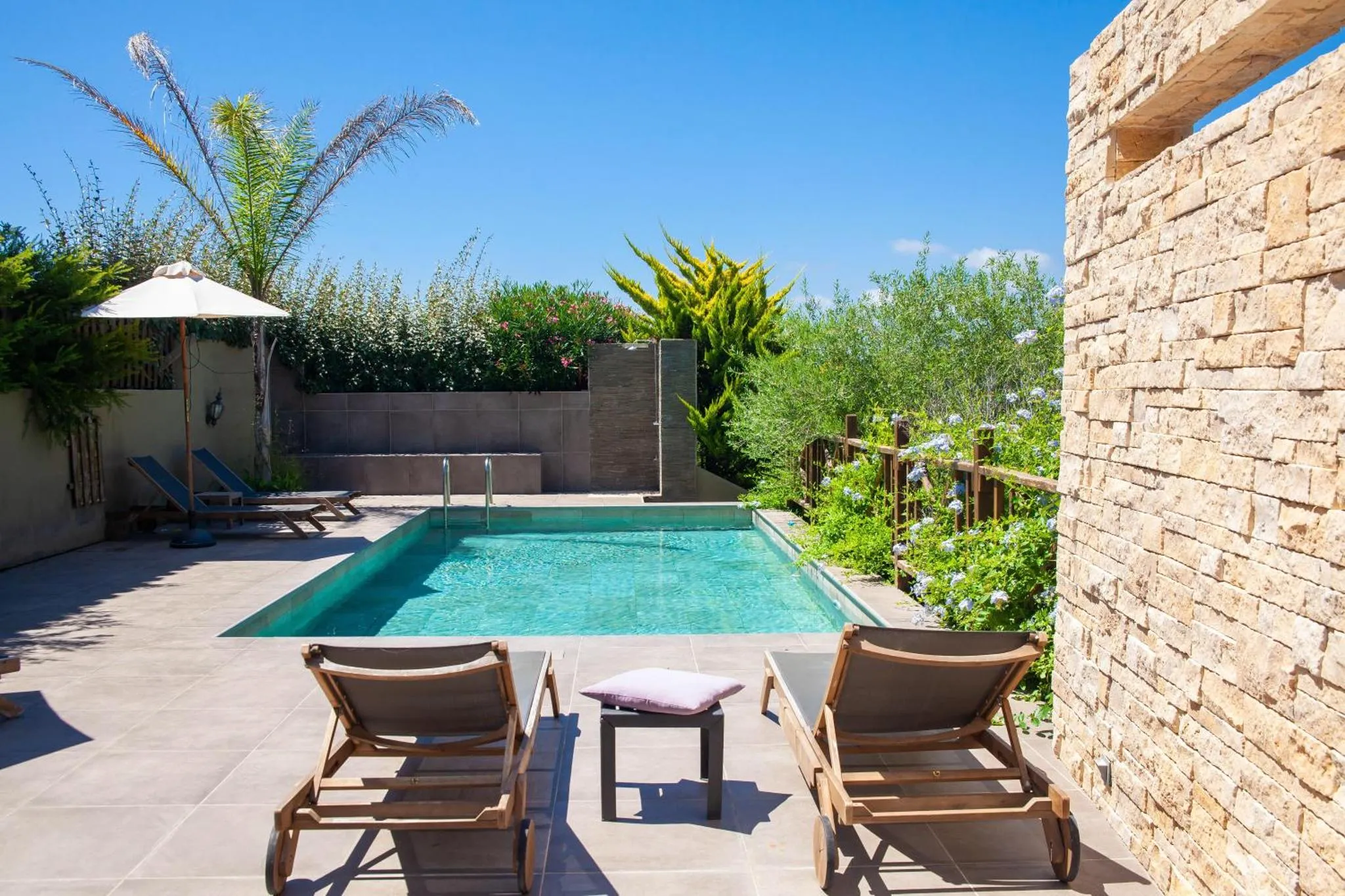 Transats et parasol bordent une piscine rectangulaire dans un jardin soigné.