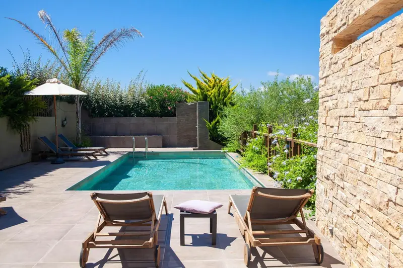 Transats et parasol bordent une piscine rectangulaire dans un jardin soigné.