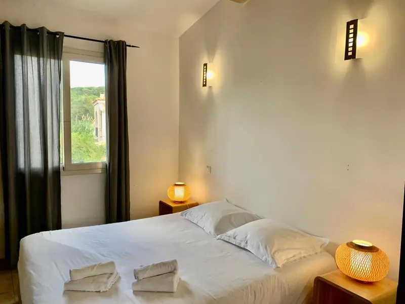Une chambre lumineuse avec un lit recouvert de blanc et des rideaux foncés.