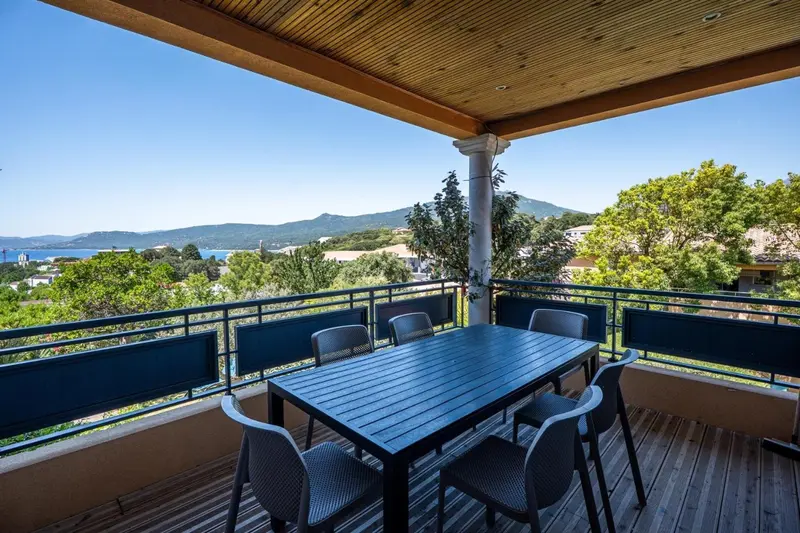 Terrasse ombragée avec table et chaises donnant sur un paysage côtier.