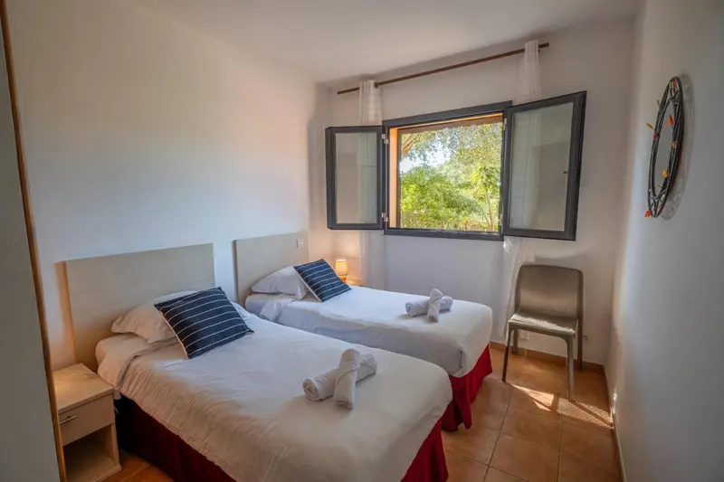 Chambre lumineuse avec deux lits simples et vue sur la végétation.