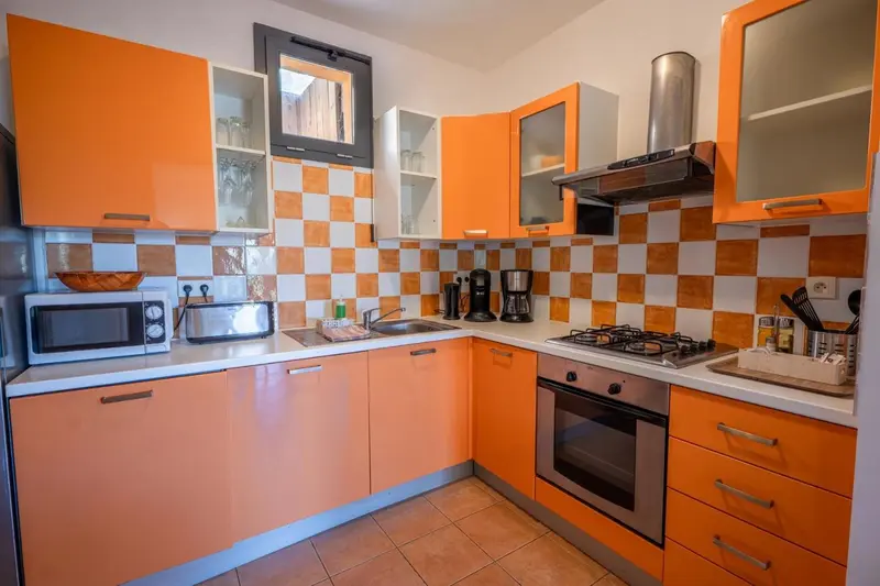 Une cuisine moderne aux meubles orange et au carrelage coloré est équipée d'appareils électroménagers.