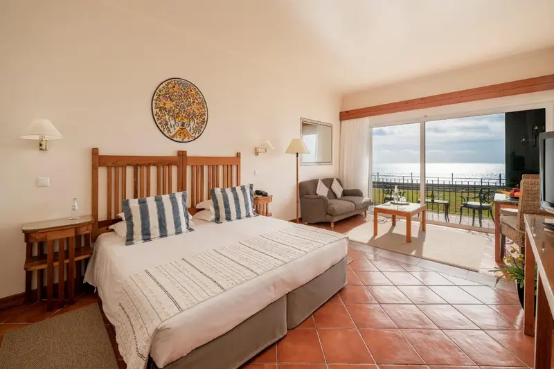Une chambre lumineuse avec un lit fait et un coin salon donnant sur une vue mer.