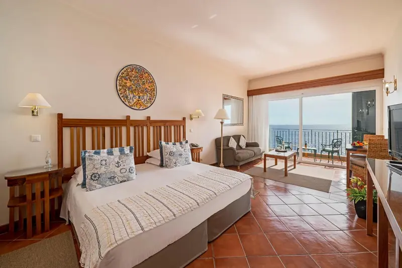 Une chambre lumineuse avec un grand lit et un coin salon donnant sur une vue mer.