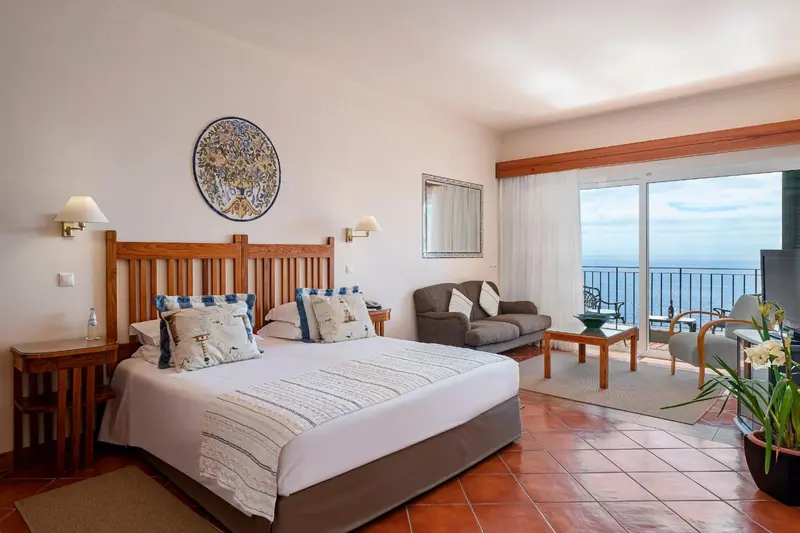 Une chambre lumineuse avec un grand lit et un coin salon donnant sur une vue mer.