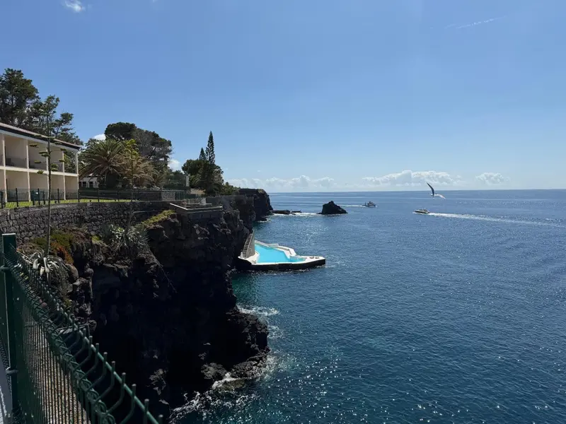 Vue d'une piscine naturelle rocheuse bordée de falaises et de végétation luxuriante.
