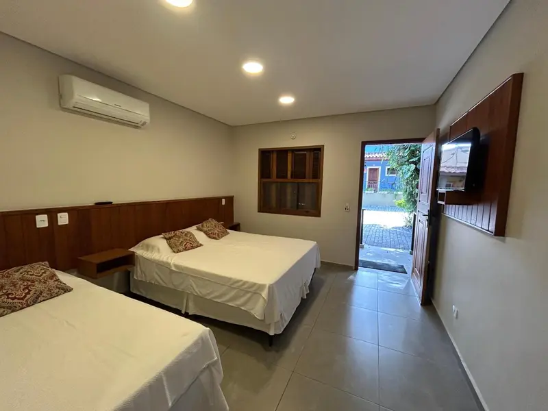 Chambre lumineuse avec deux lits simples et une porte ouverte sur une cour.