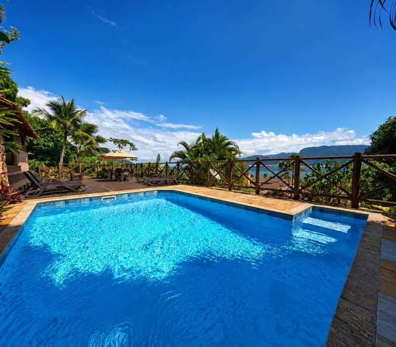 Une piscine turquoise bordée d'une terrasse ensoleillée offre une vue sur la mer et les montagnes.