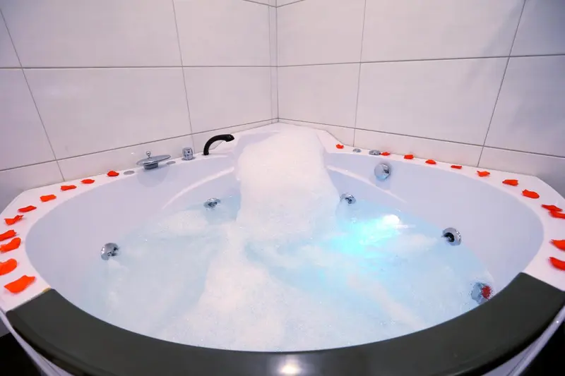 Baignoire d'angle remplie d'eau et décorée de pétales de fleurs.