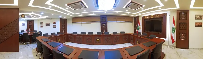 Une grande table de réunion en bois est entourée de chaises dans une salle décorée de boiseries et de tableaux.