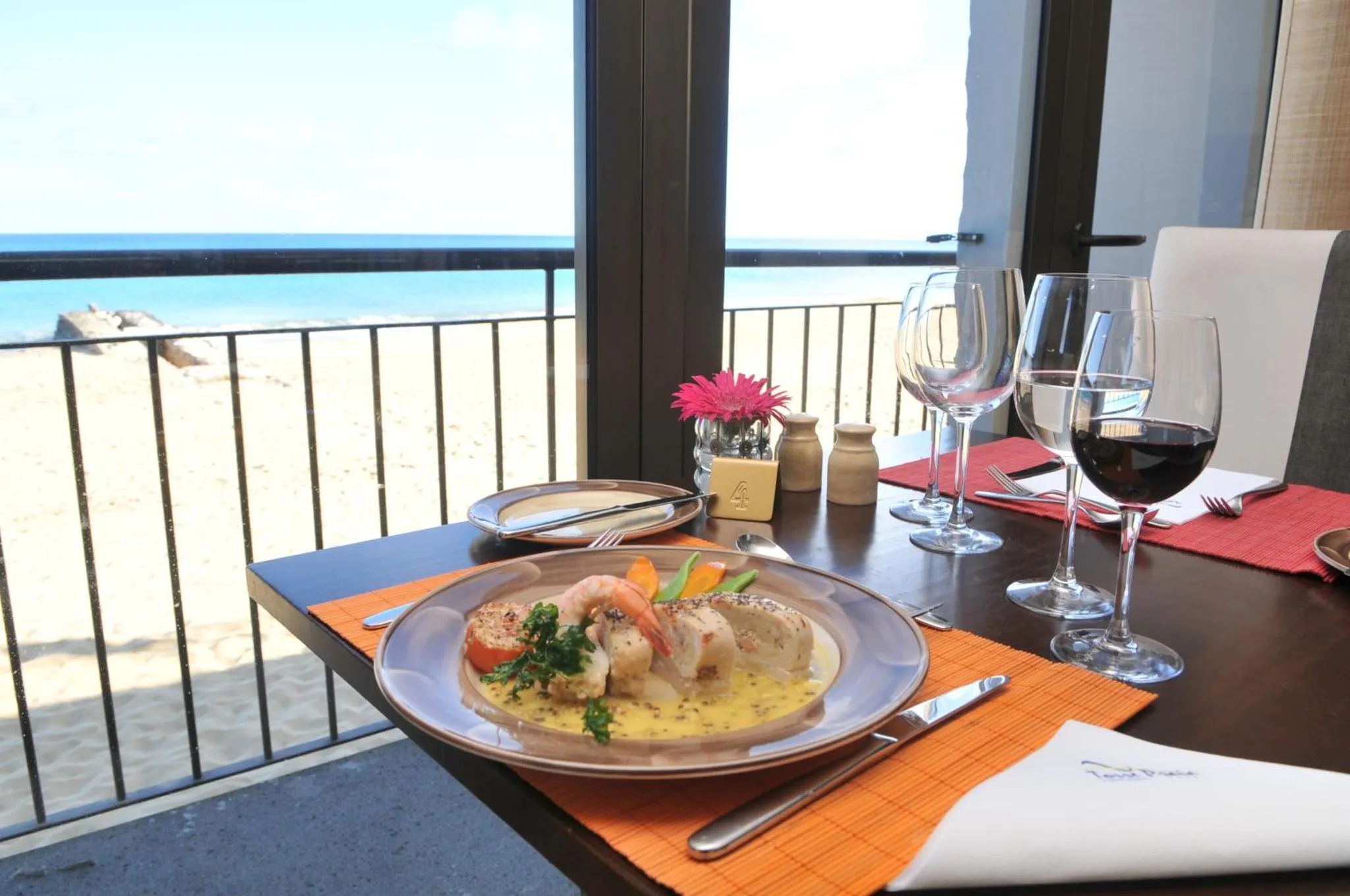 Une table est dressée avec un plat de fruits de mer et des verres de vin, face à une vue sur la mer.
