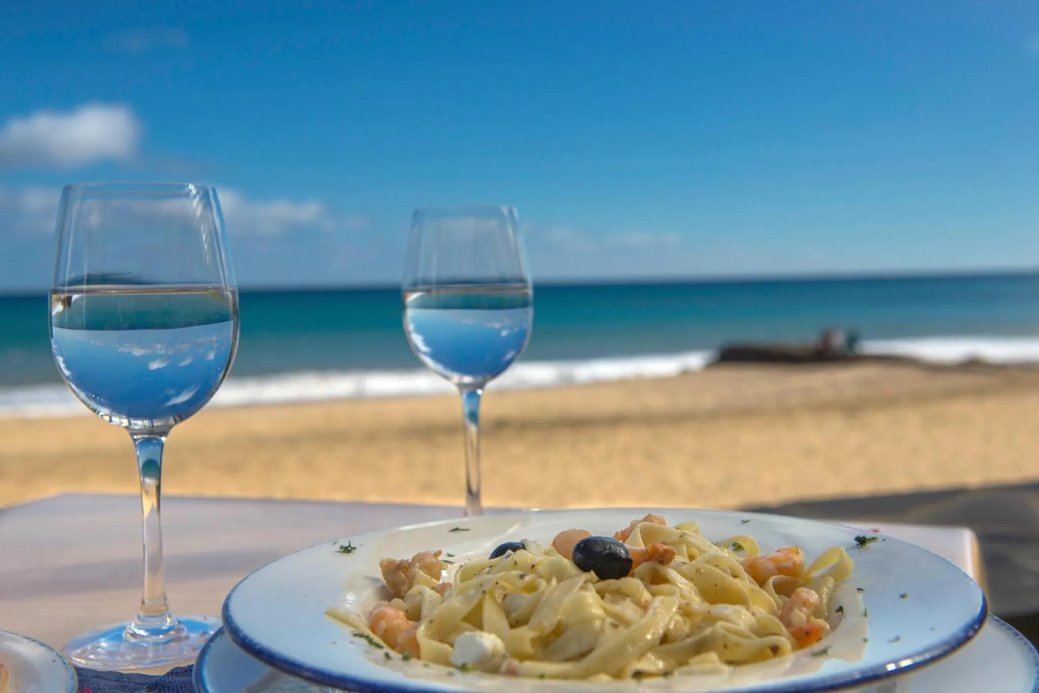Une assiette de pâtes et deux verres d'eau sont disposés sur une table en bord de mer.