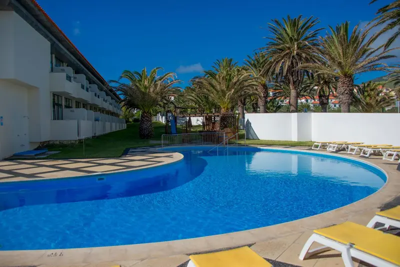 Piscine rectangulaire entourée de chaises longues et de végétation tropicale.
