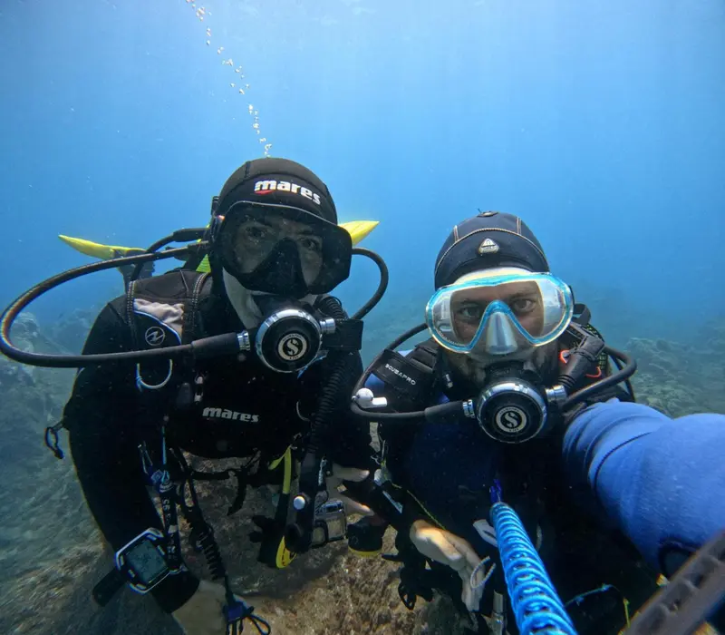Deux plongeurs sourient face à l'objectif dans une eau turquoise.