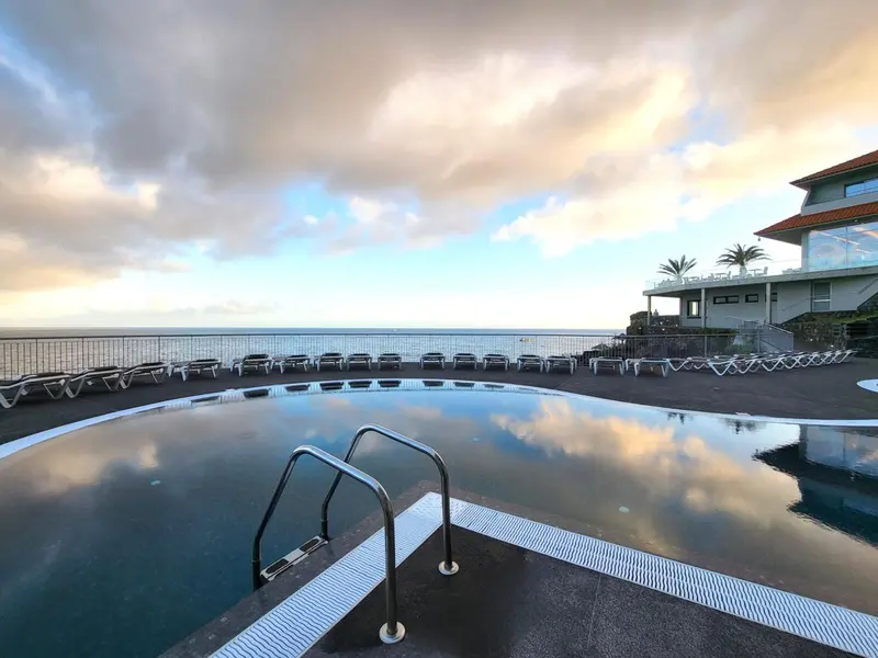 Une piscine à débordement reflète le ciel nuageux et la mer.