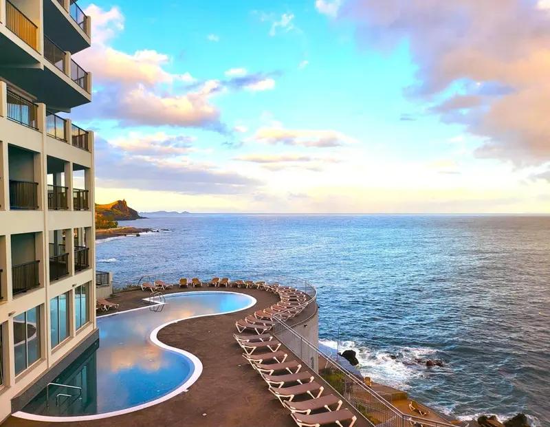 Vue d'une piscine d'hôtel surplombant la mer au coucher du soleil.