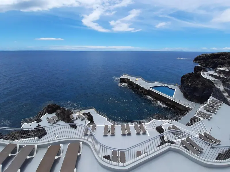 Terrasse ensoleillée avec transats surplombant une piscine naturelle et l'océan.