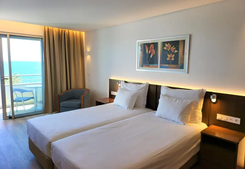 Une chambre lumineuse avec un grand lit et un balcon donnant sur la mer.