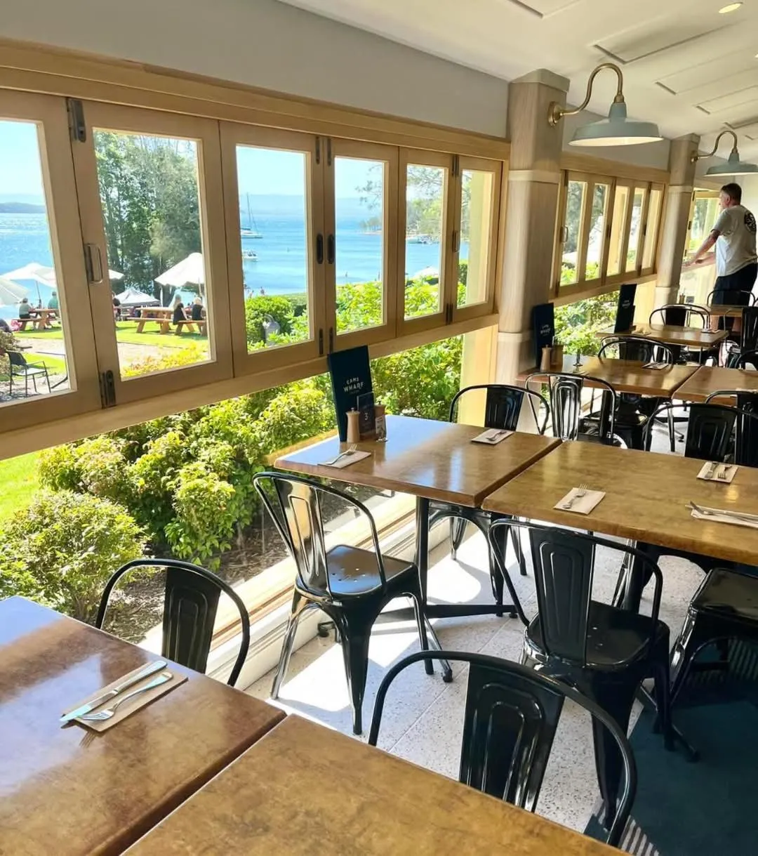 Une salle lumineuse avec de grandes baies vitrées donnant sur la mer et un jardin.