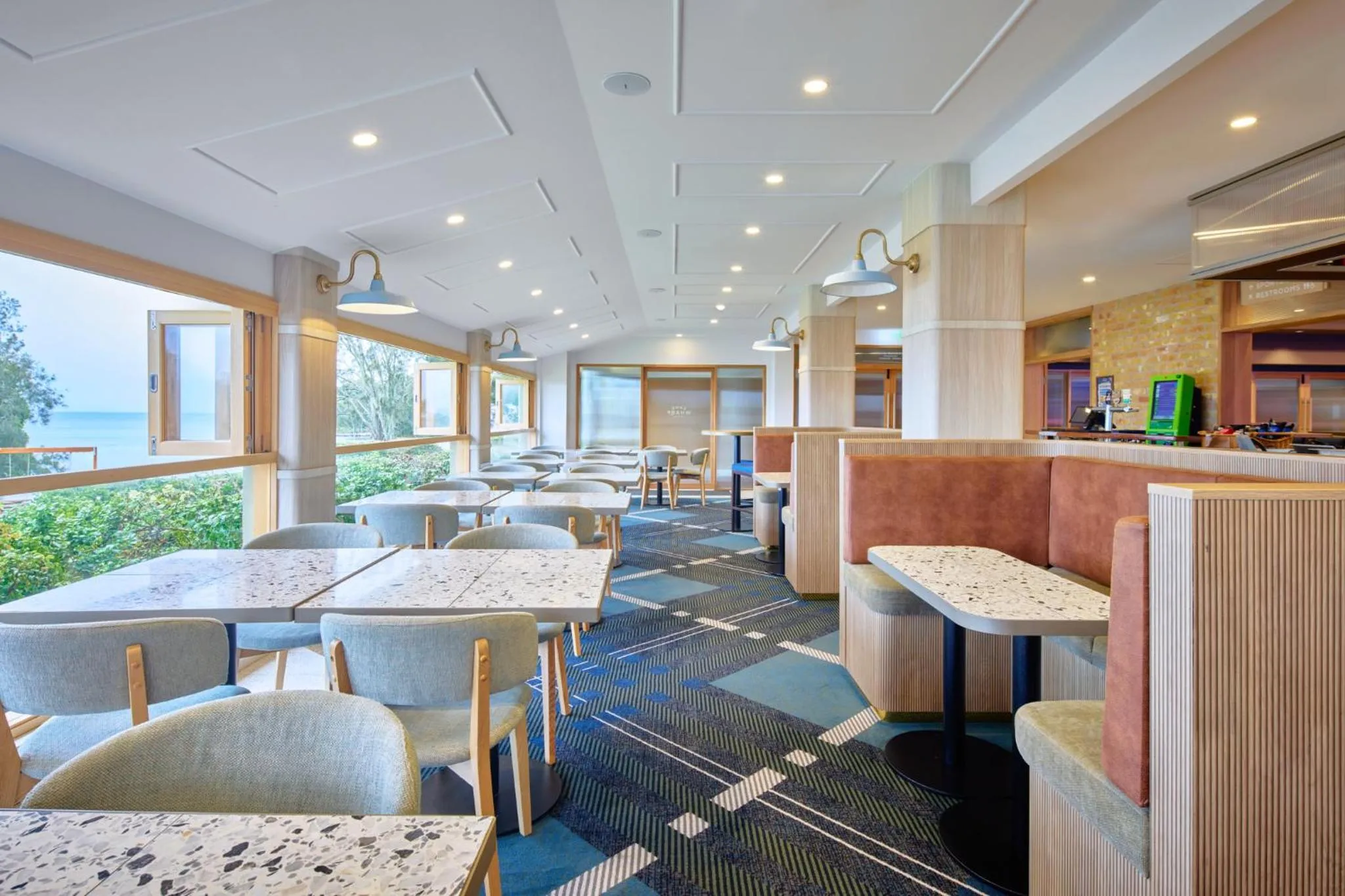 Une salle lumineuse avec des tables et des banquettes près de grandes fenêtres donnant sur la mer.