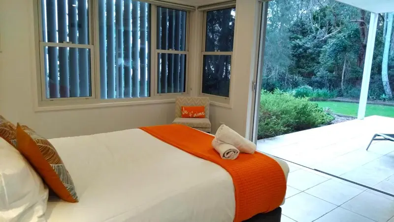 Une chambre lumineuse avec un lit recouvert d'une couverture orange et un accès à une terrasse.