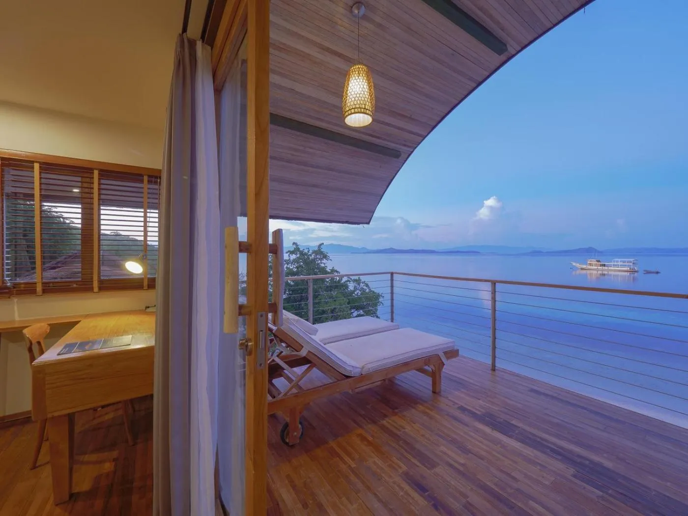 Terrasse en bois avec chaises longues donnant sur la mer au crépuscule.