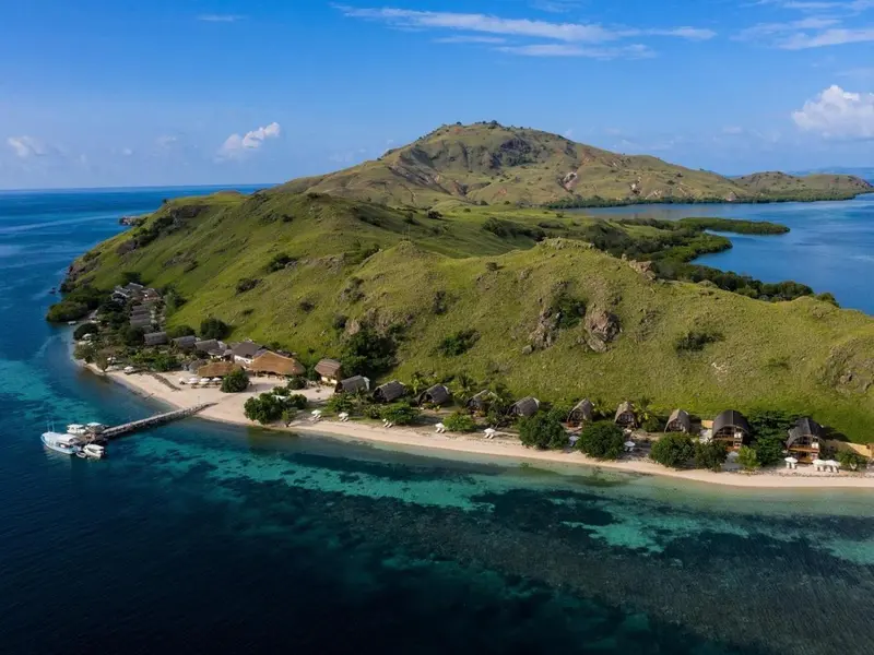 Vue aérienne d'une île tropicale avec des bungalows sur une plage de sable fin.