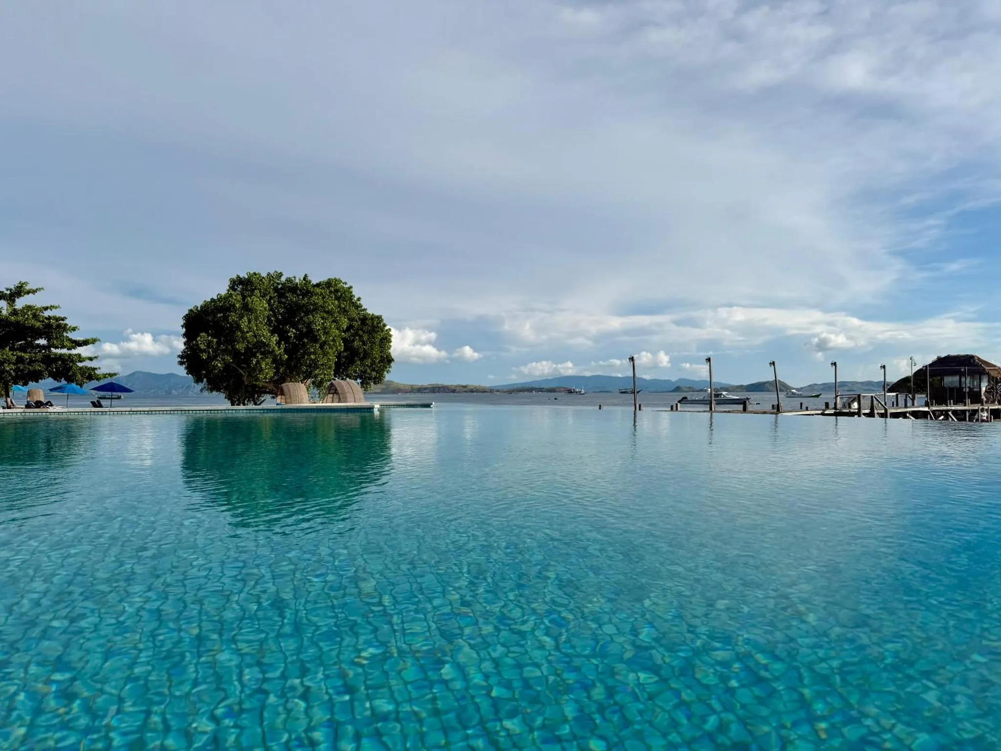 Piscine à débordement turquoise face à la mer sous un ciel nuageux.