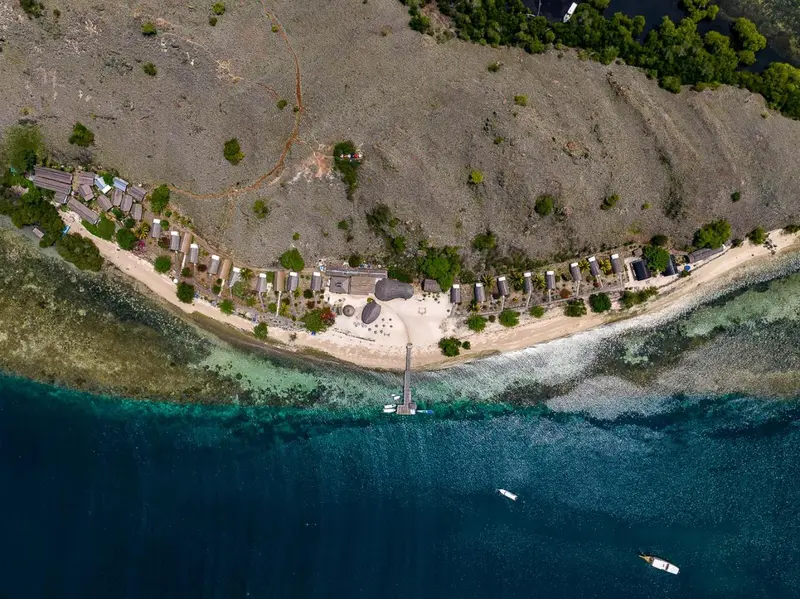 Vue aérienne d'une plage bordée de bungalows et d'une eau turquoise.
