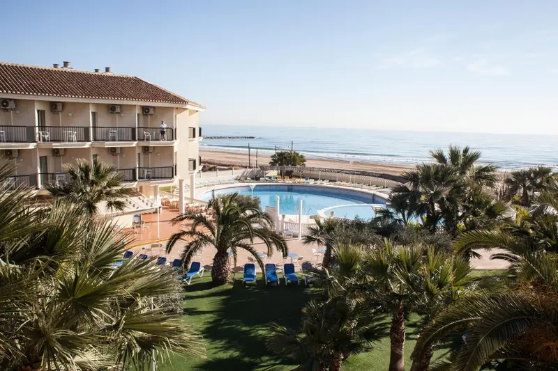Vue aérienne d'un bâtiment beige avec des balcons donnant sur une piscine et la mer.