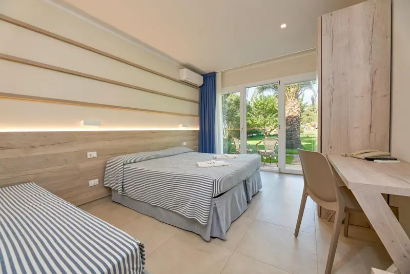 Une chambre lumineuse avec un lit double et un bureau donnant sur un jardin.