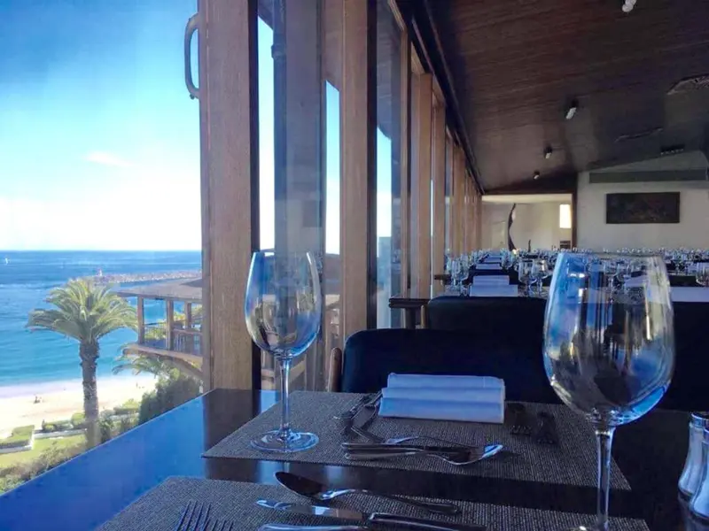 Une table est dressée devant une grande baie vitrée donnant sur la mer.