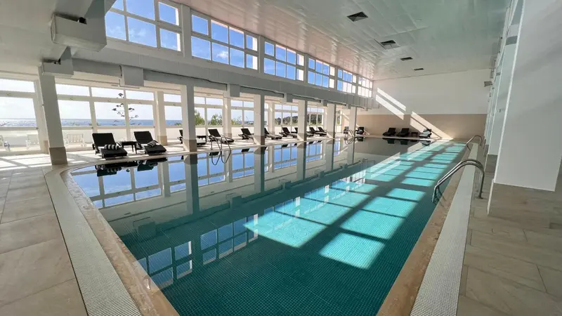 Une piscine intérieure lumineuse avec des transats alignés le long d'une baie vitrée.