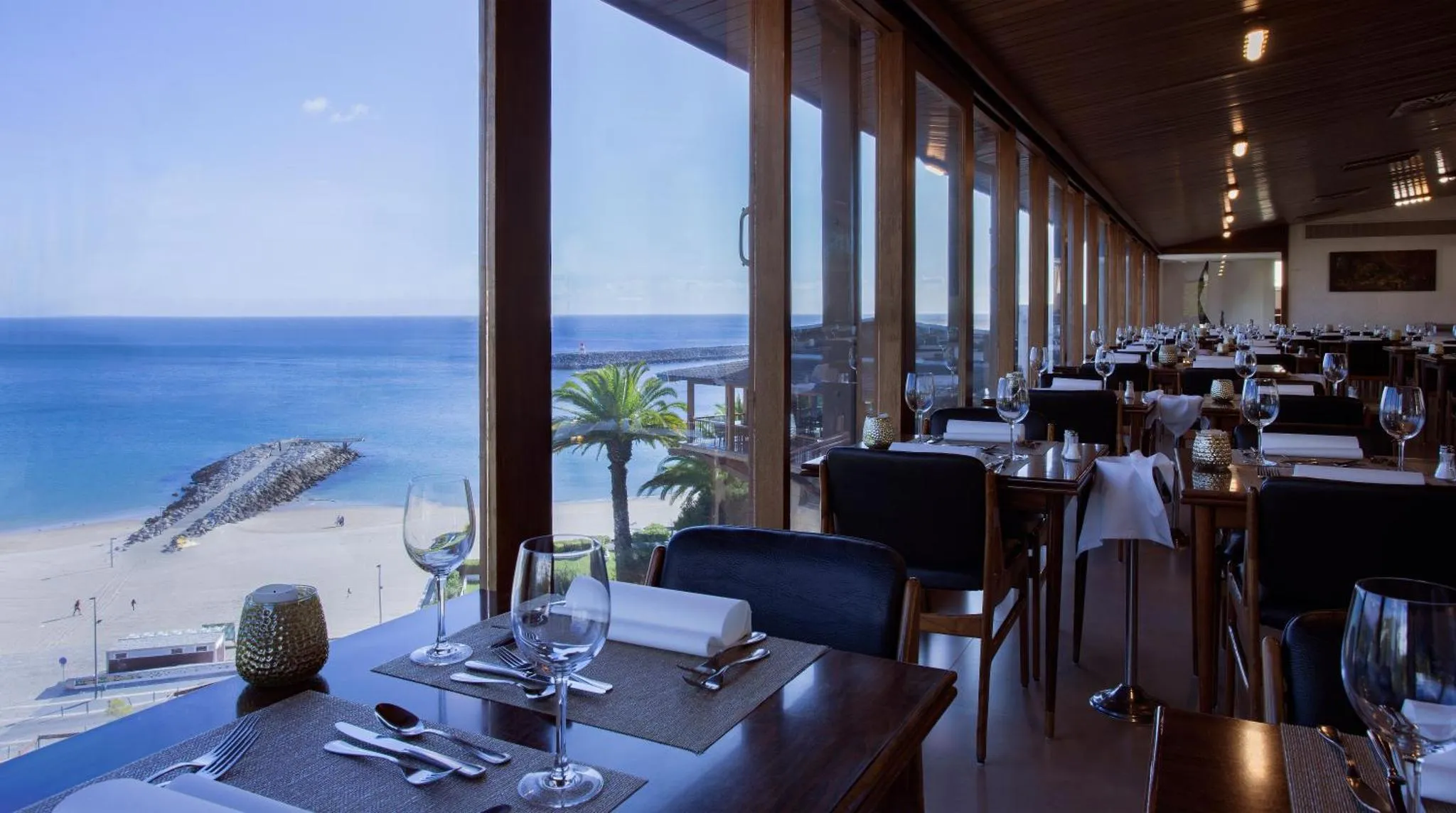 Une table dressée avec des couverts et des verres offre une vue sur la mer et la plage.
