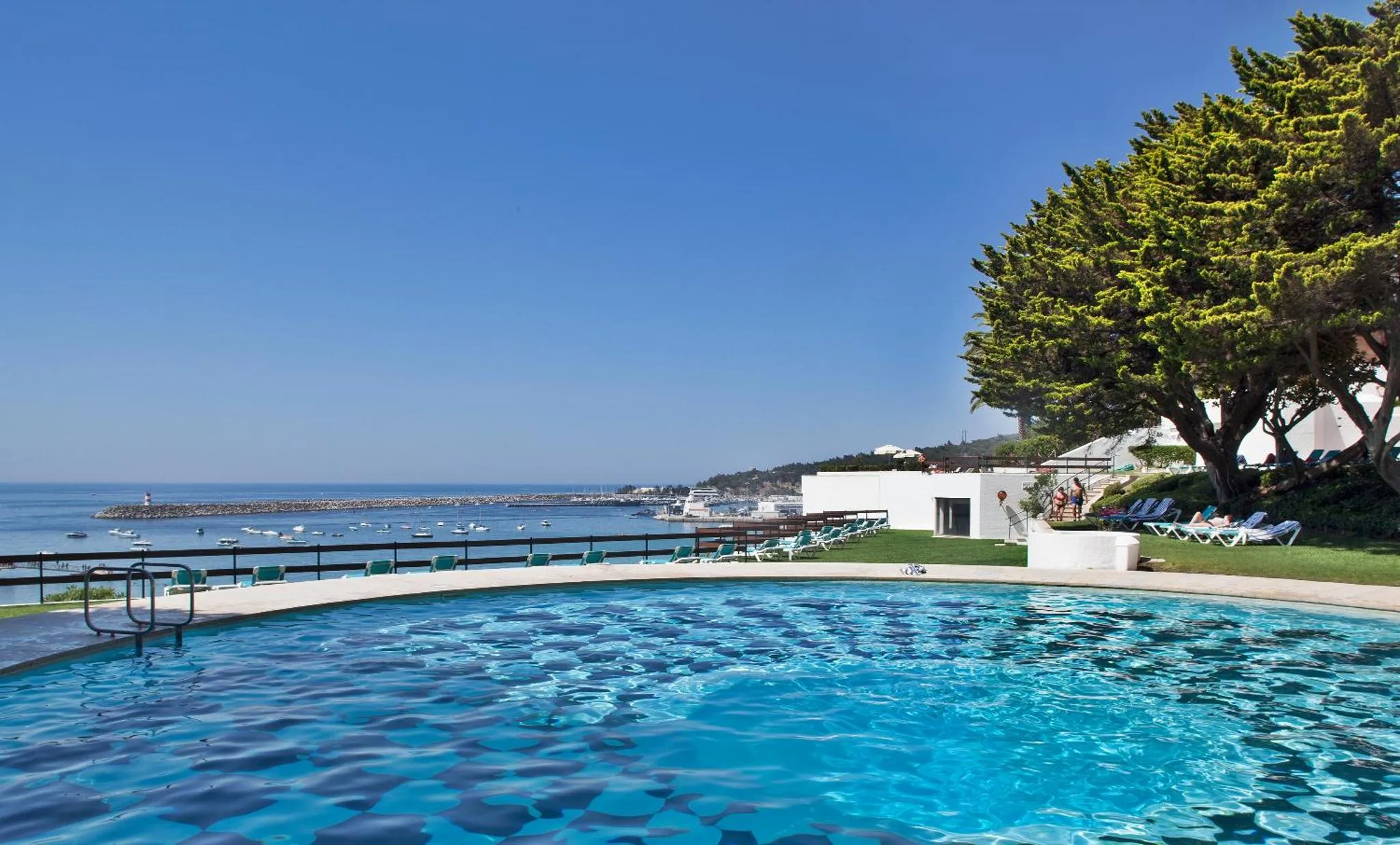 Une piscine bleue au premier plan surplombe une vue sur la mer et la côte.