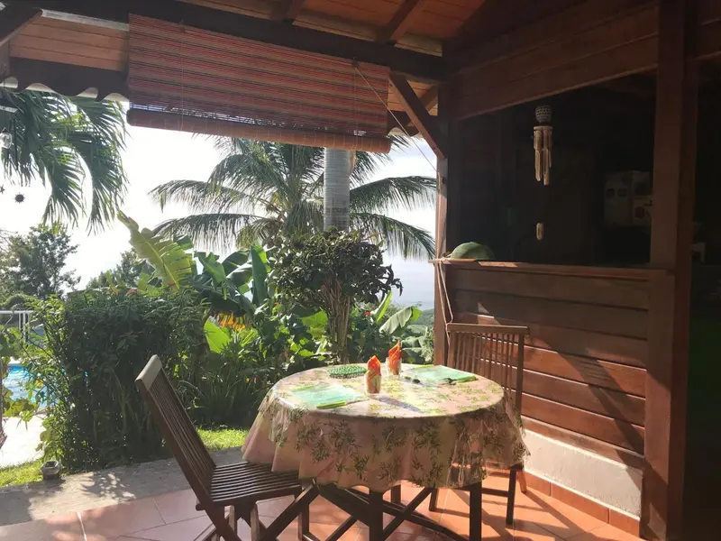 Une table ronde est mise en scène sur une terrasse ombragée avec une vue sur la végétation.