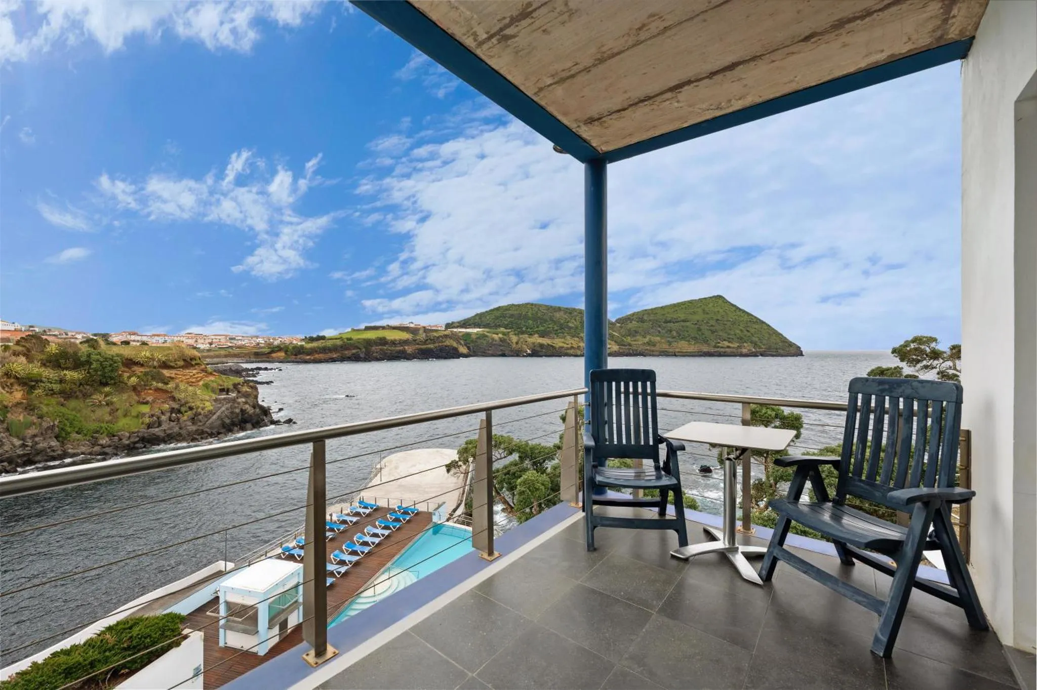 Deux fauteuils et une petite table sur une terrasse avec vue sur la mer et la côte.