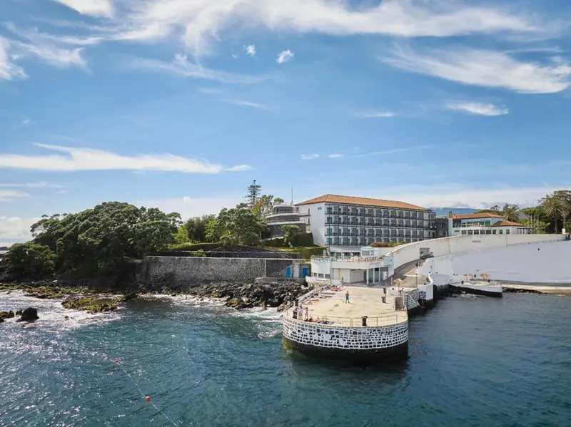 Bâtiment blanc surplombant une jetée rocheuse et la mer.