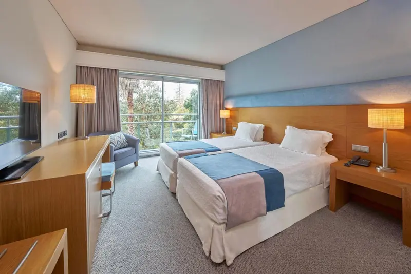 Chambre lumineuse avec deux lits simples et vue sur la végétation.