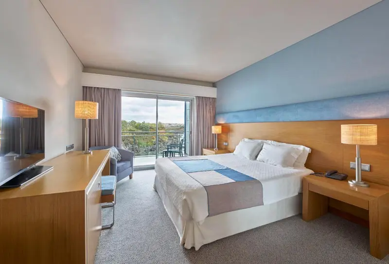 Chambre lumineuse avec un grand lit et vue sur l'extérieur.