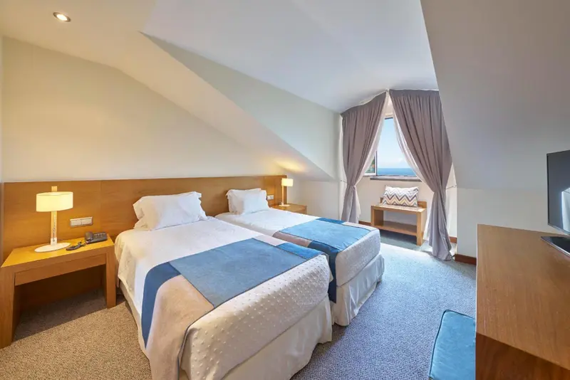 Chambre lumineuse avec deux lits simples et une fenêtre donnant sur la mer.