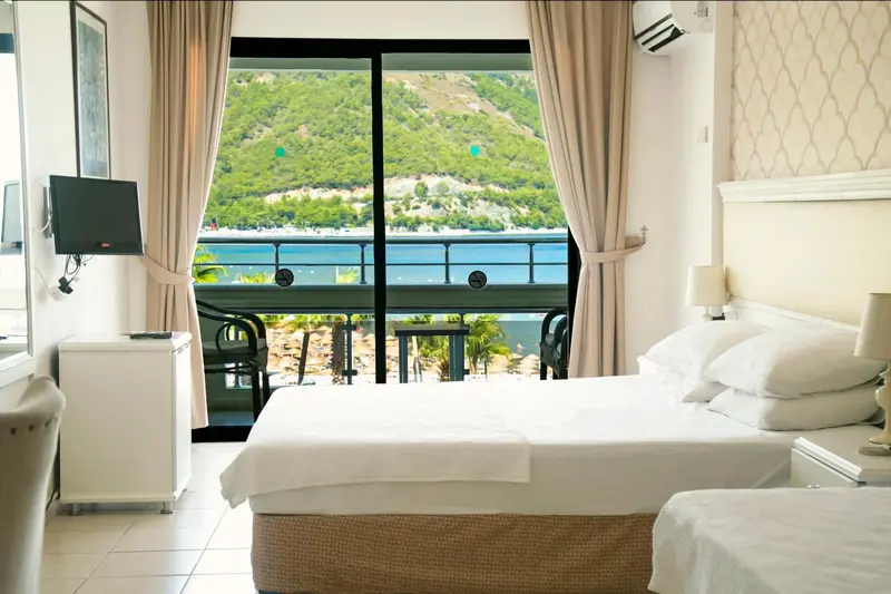 Une chambre lumineuse avec un grand lit donnant sur une vue mer et montagne.
