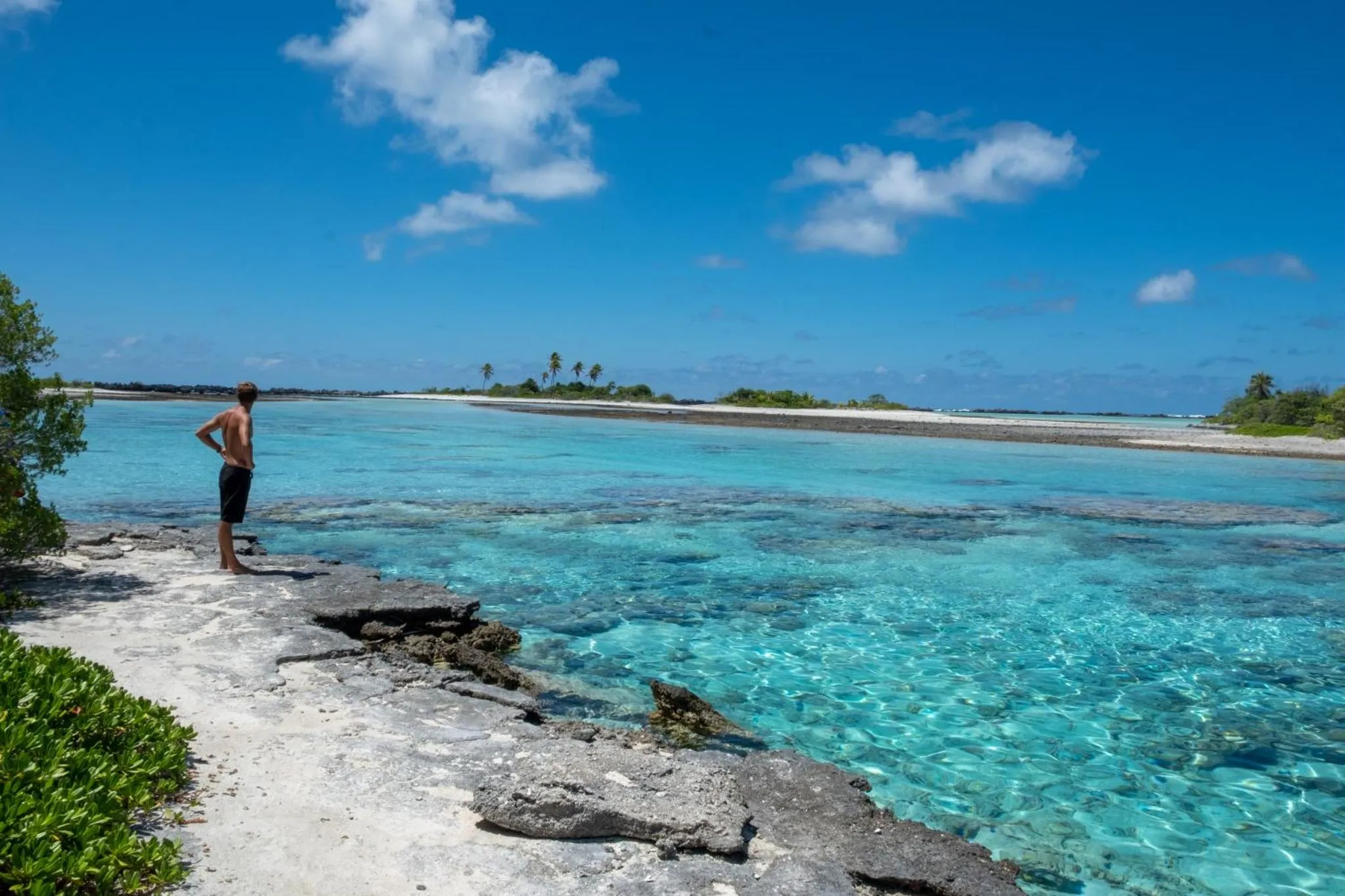 Un homme se tient sur un rivage rocheux face à un lagon turquoise.