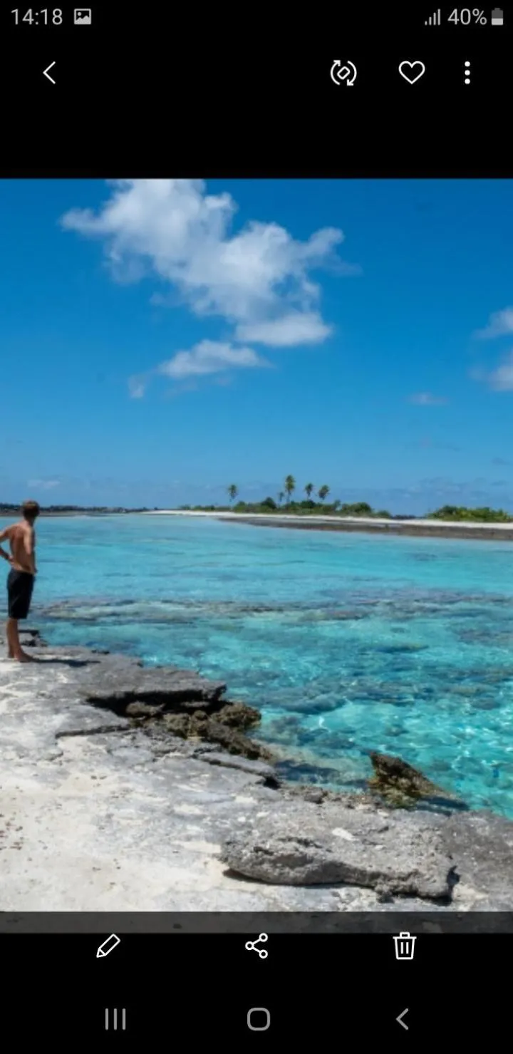 Un homme se tient sur un rivage rocheux face à un lagon turquoise.