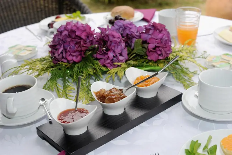 Une table est dressée avec des confitures, des viennoiseries et des boissons.